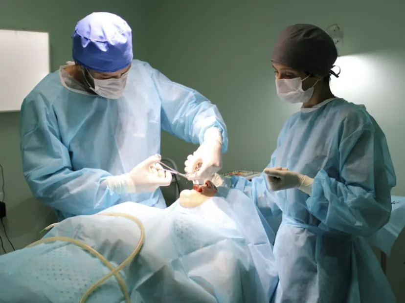 Cirurgião e auxiliar em procedimento, com aventais cirúrgicos