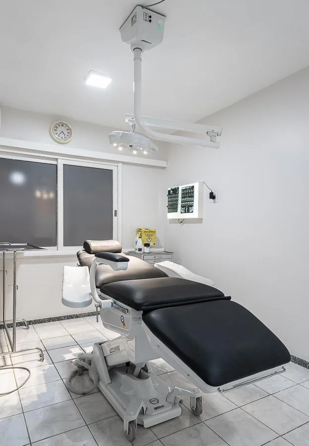 Sala cirúrgica com cadeira reclinável preta e foco cirúrgico no teto