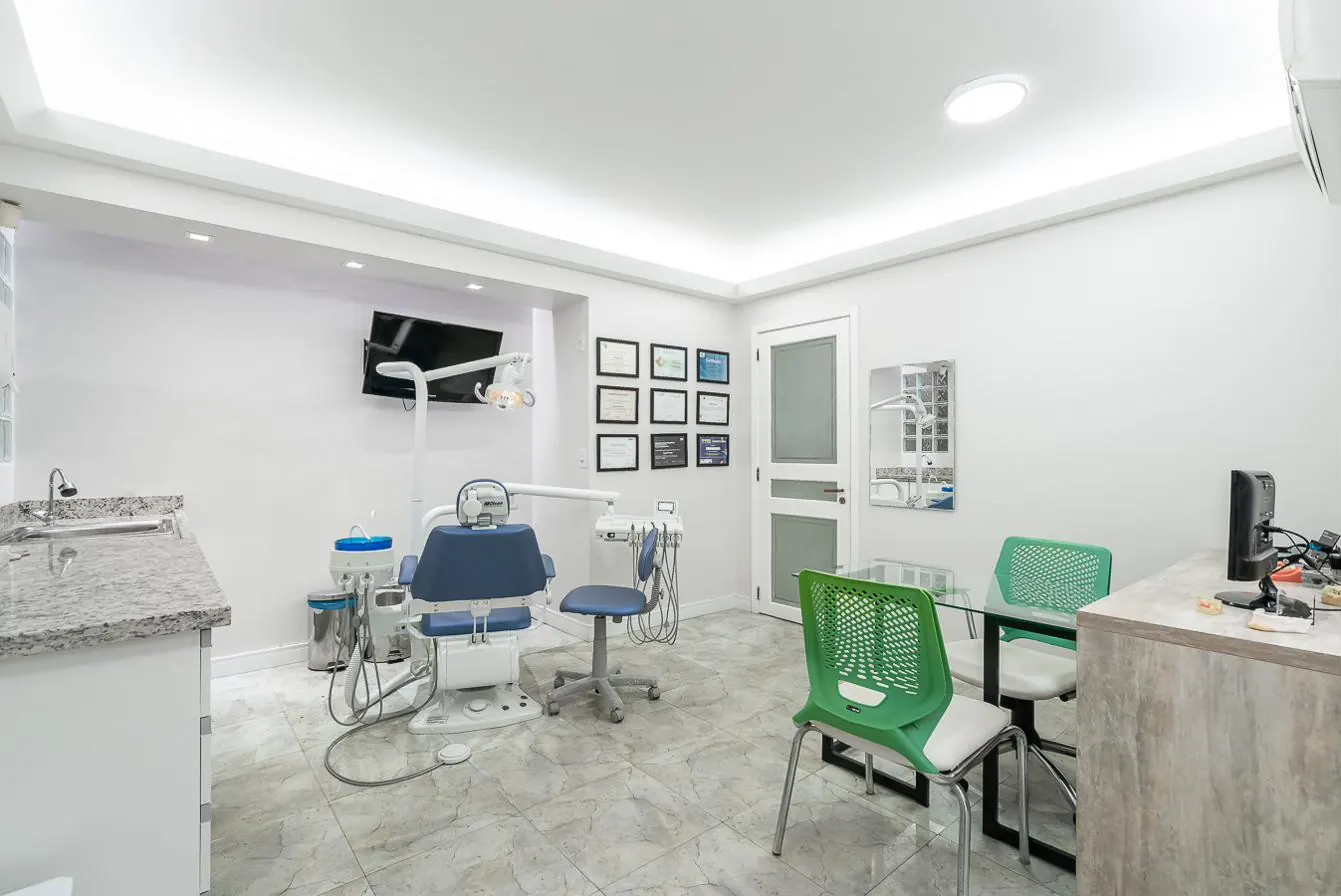 Consultório com cadeira odontológica azul e diplomas na parede