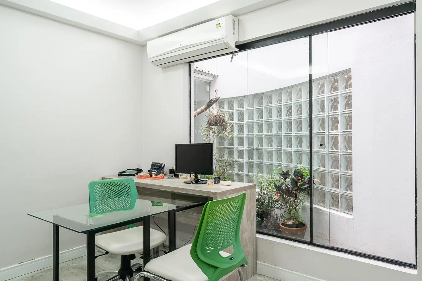 Sala de atendimento com mesa de vidro, cadeiras verdes e jardim interno