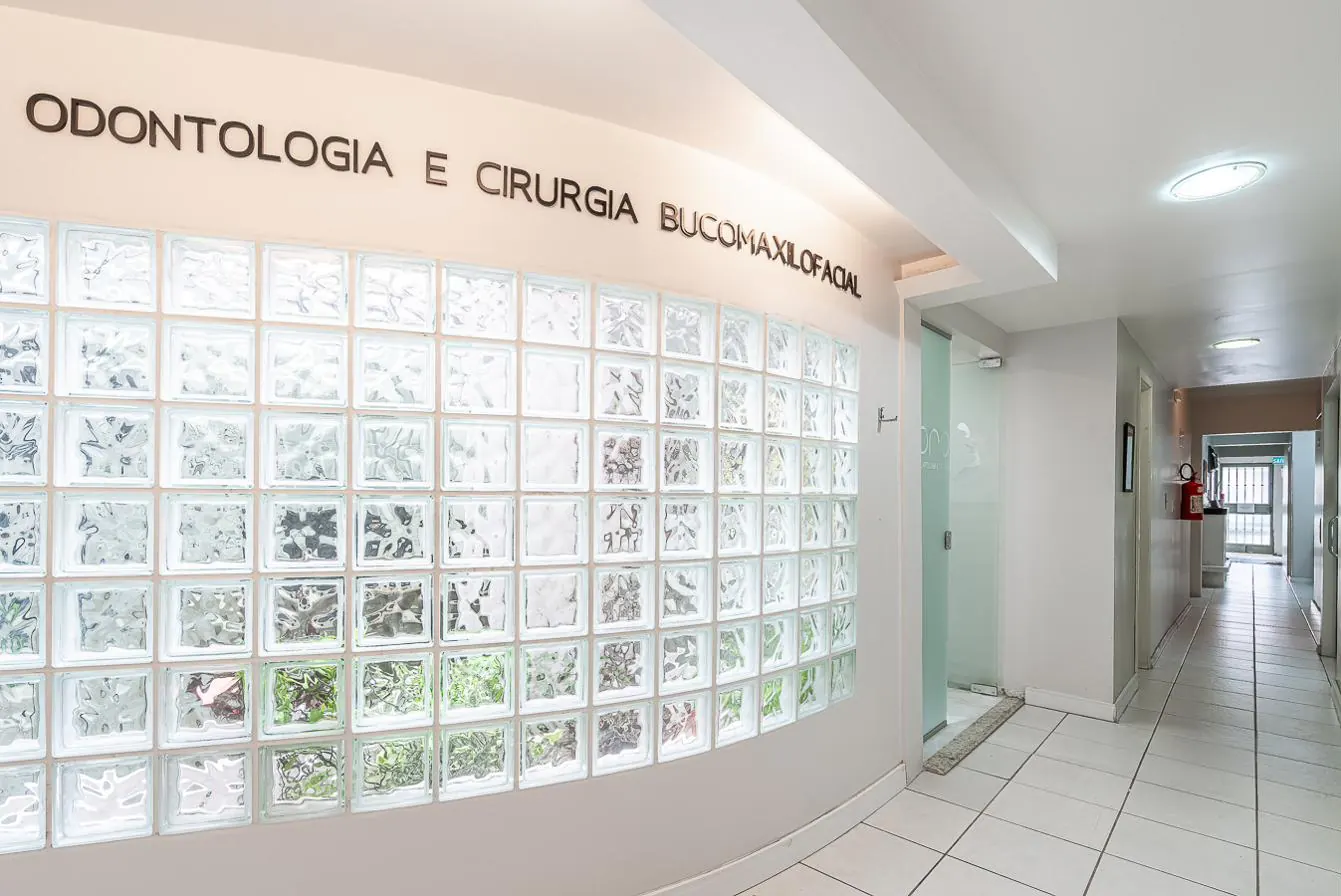 Corredor com parede curva de blocos de vidro e o letreiro Odontologia e Cirurgia Bucomaxilofacial
